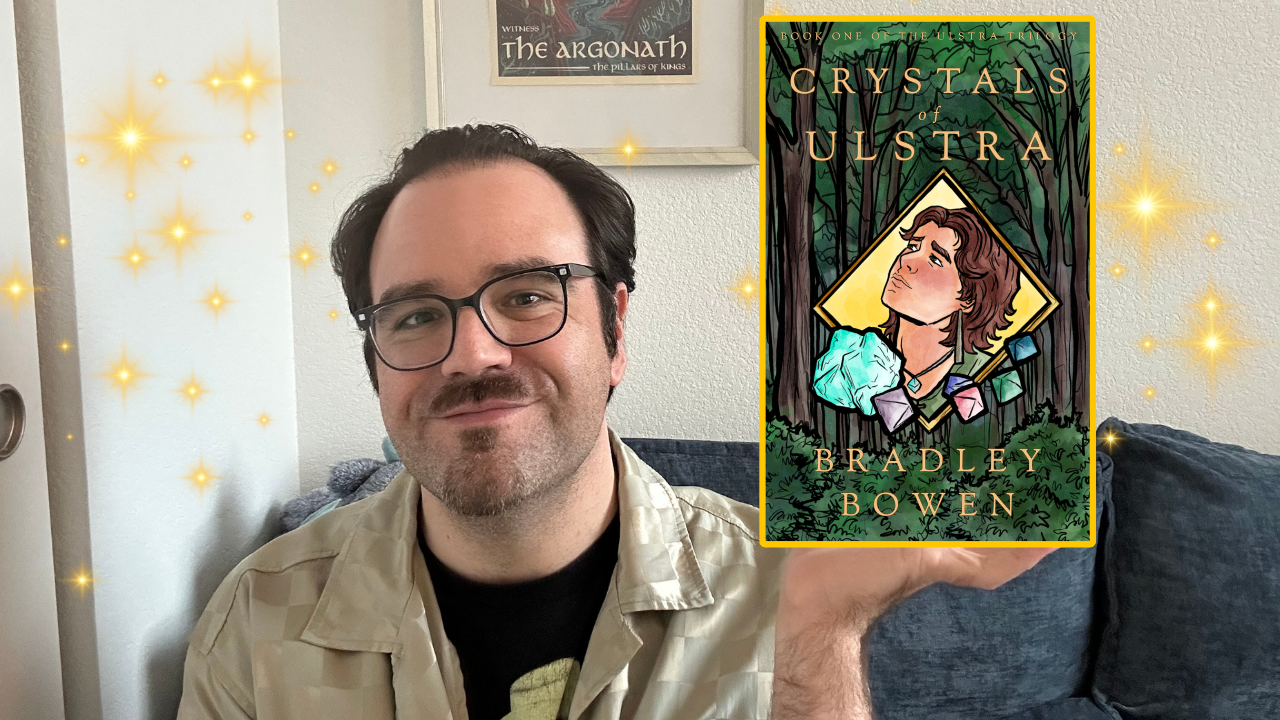 A photograph of author Bradley Bowen displaying the cover of his queer fantasy book Crystals of Ulstra.